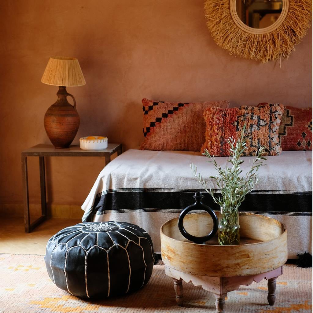Decoración marroquí con cojines de sabra bordados a mano, pufs de cuero artesanales y una alfombra tradicional, creando un ambiente acogedor y auténtico.
