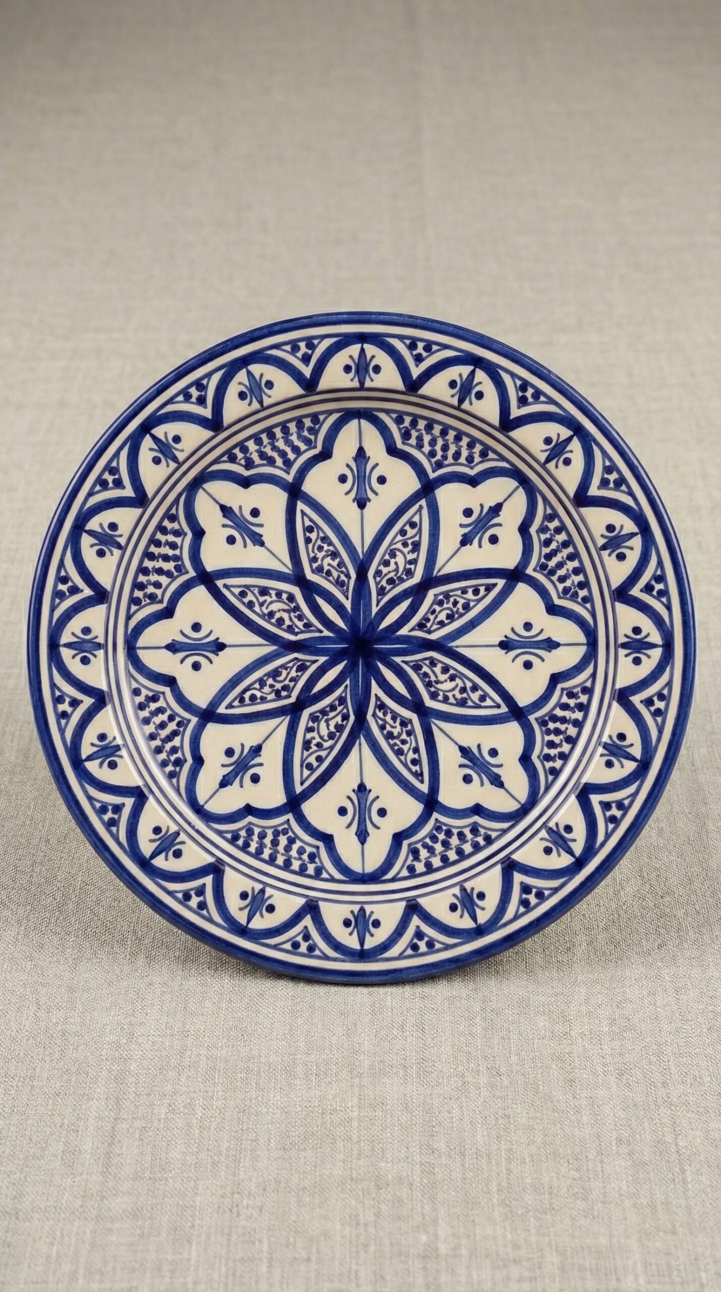 Plato de cerámica marroquí de 21cm pintado a mano. Diseño geométrico floral en tonos azul claro, coral y azafrán sobre fondo blanco crema. Acabado esmaltado brillante